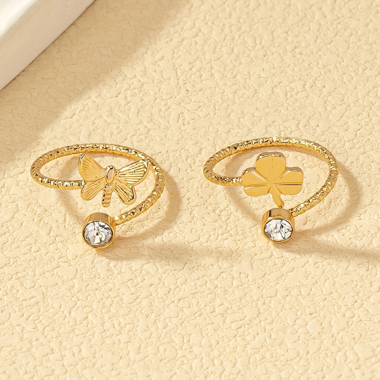 Two gold rings with butterfly and clover designs on a beige background - Affordable Artificial jewellery in pakistan