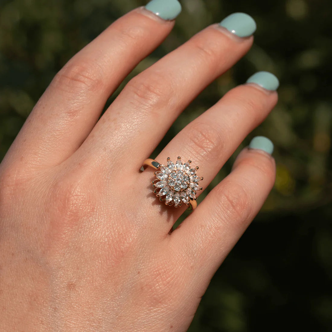 Hand wearing a diamond ring with a blurred green background