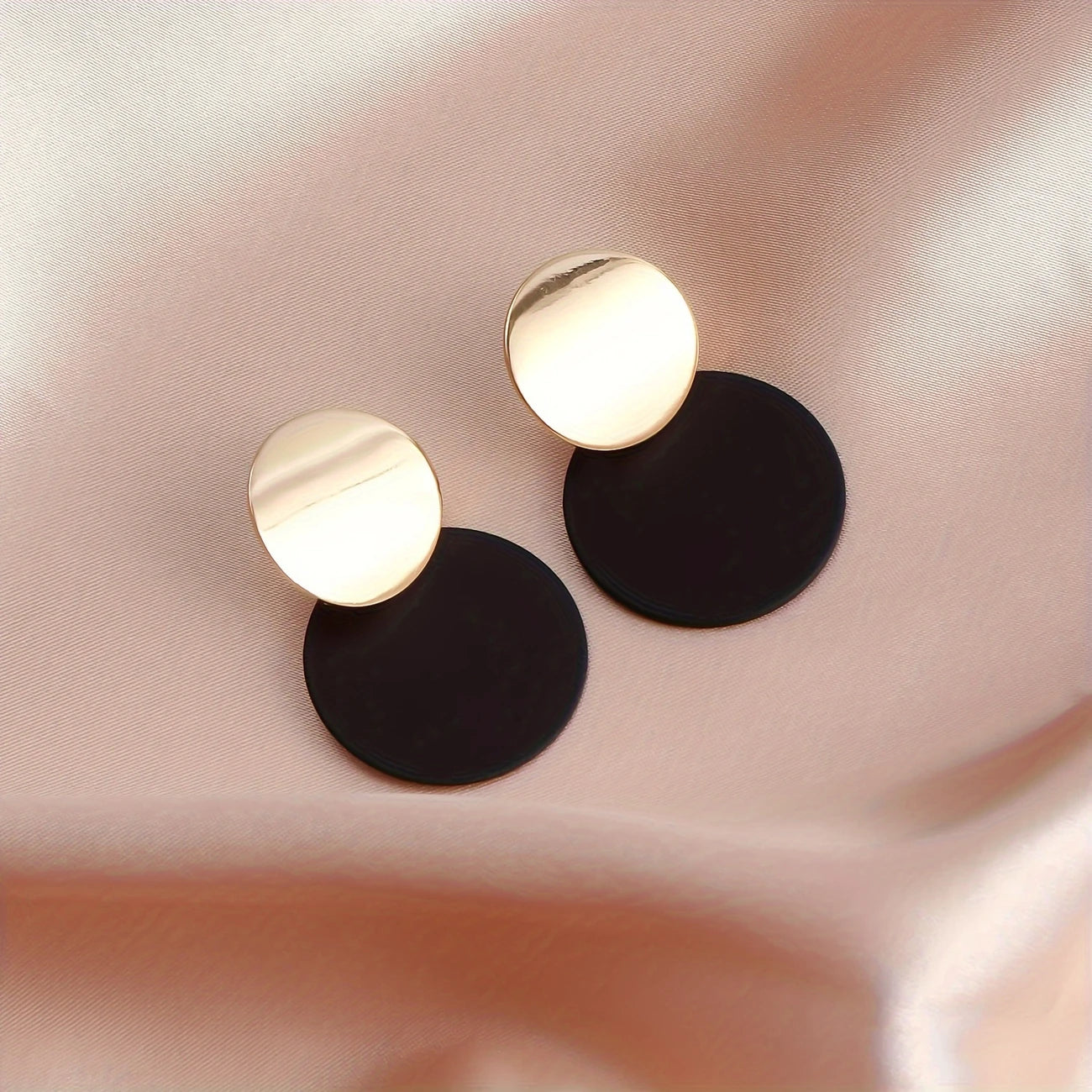 Pair of gold and black round earrings on a soft pink fabric background - stylish Korean jewellery in Pakistan