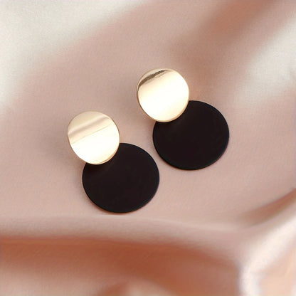 Pair of gold and black round earrings on a soft pink fabric background - stylish Korean jewellery in Pakistan