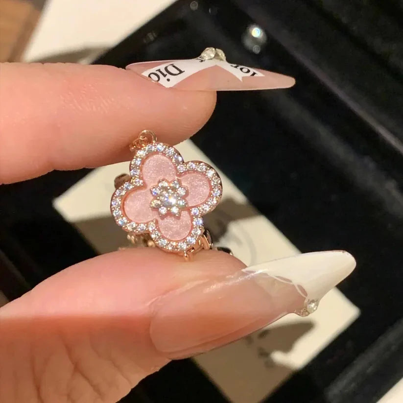 Pink flower-shaped earring held between fingers with a blurred background