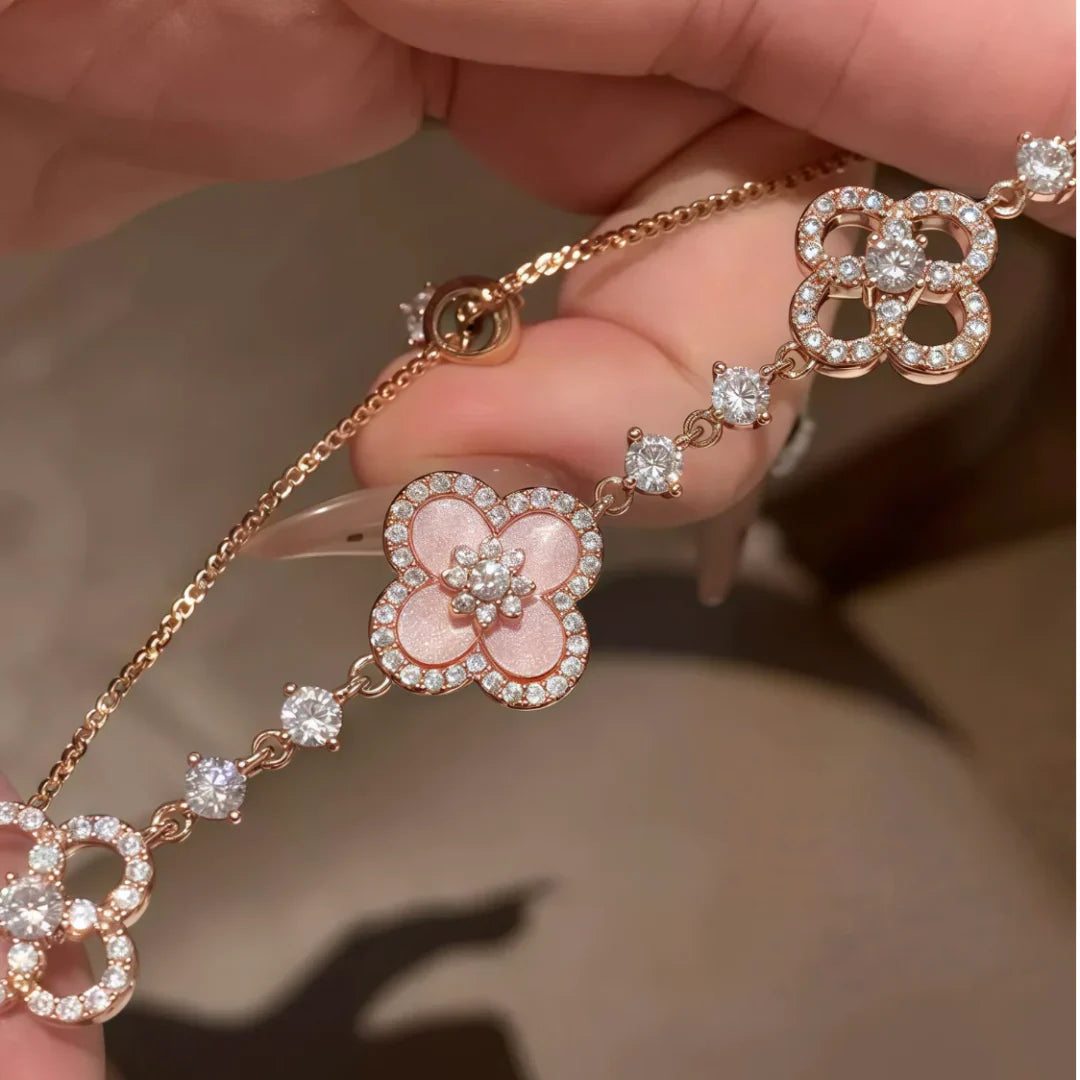 Rose gold bracelet with floral designs and diamonds held by a hand against a neutral background
