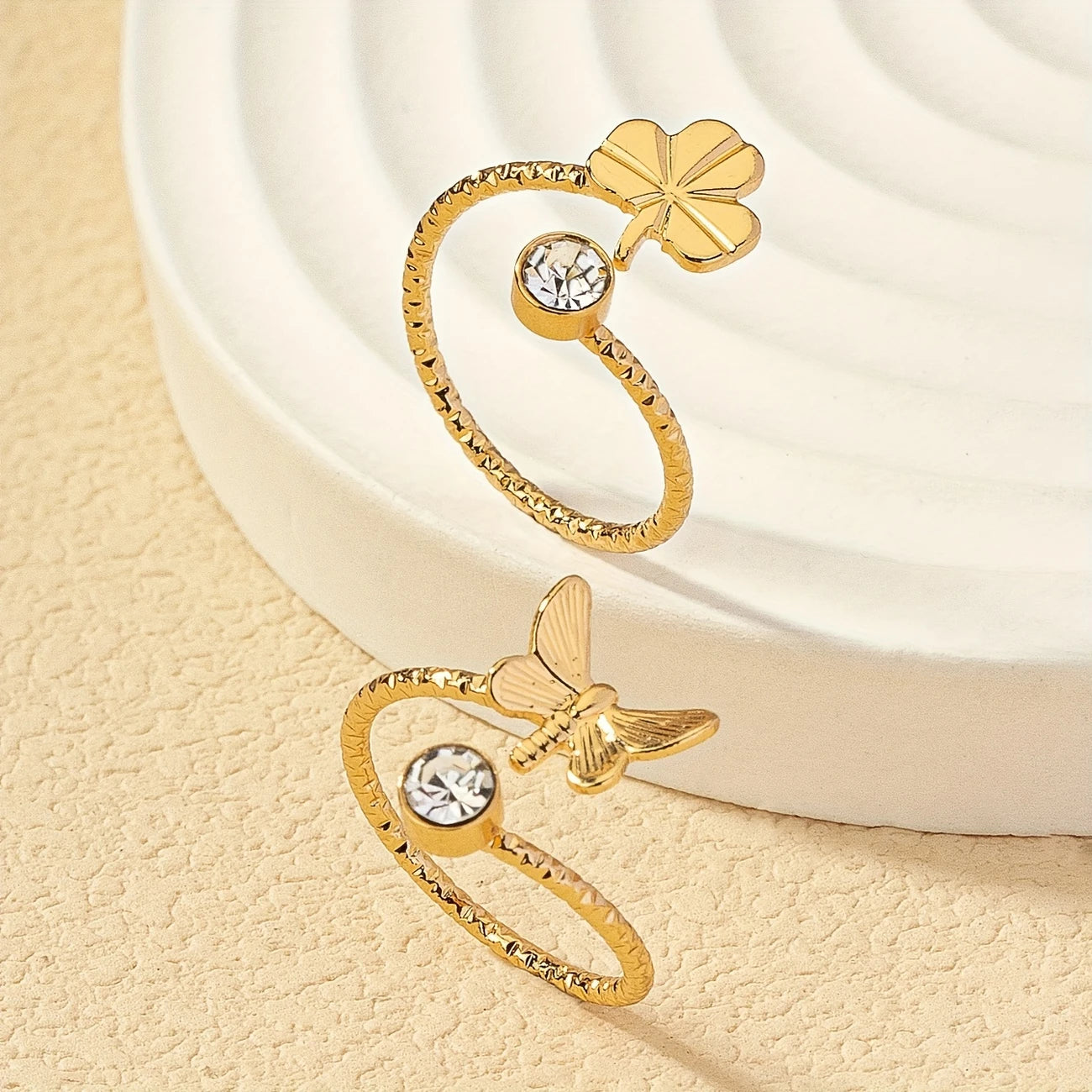 Gold open rings with clover and dragonfly designs on a beige surface - Affordable Artificial jewellery in pakistan