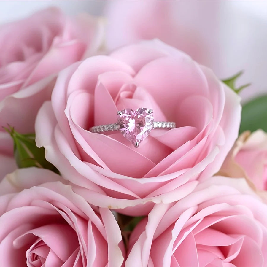 Heart-shaped diamond ring nestled in a pink rose among other pink roses.