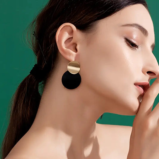 Close-up of a woman wearing gold and black earrings against a green background - affordable artificial jewellery in Pakistan