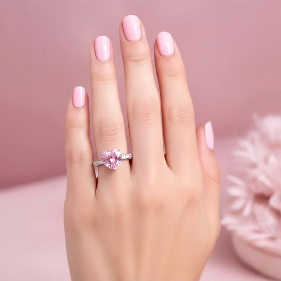 Hand wearing a pink gemstone ring with a soft pink background