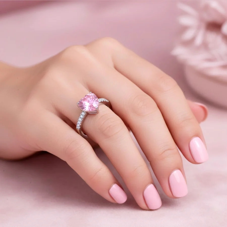 Hand wearing a pink heart-shaped ring on a soft pink background