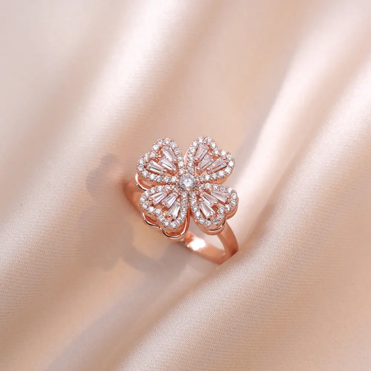 Rose gold flower-shaped ring with clear gemstones on a soft pink fabric background