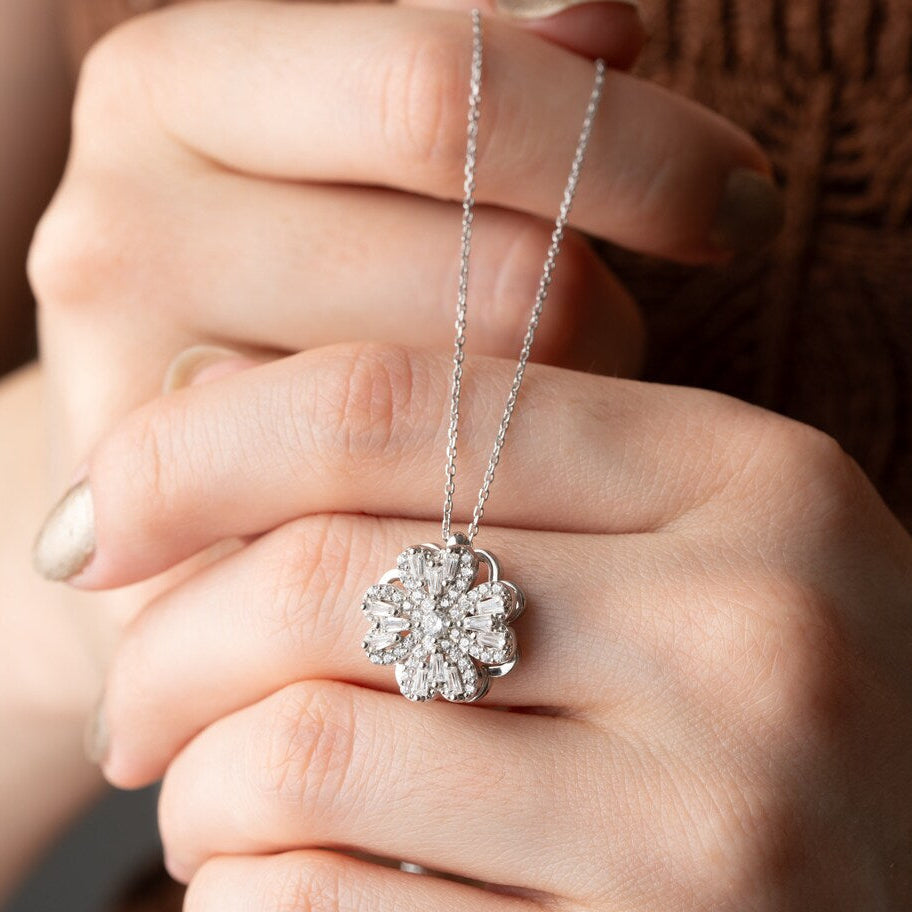Lucky Clover Spinner Necklace Close-up of a hand holding a silver necklace with a floral pendant.