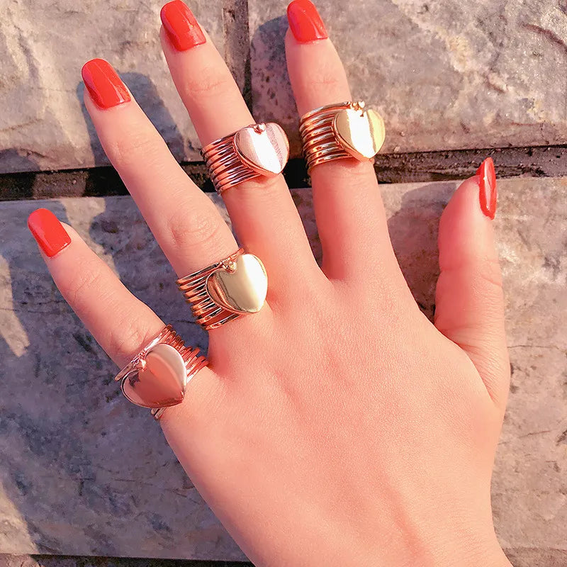 Hand wearing multiple gold rings with red nail polish on a stone surface