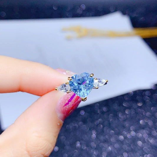 Blue gemstone ring held by a hand with a blurred background