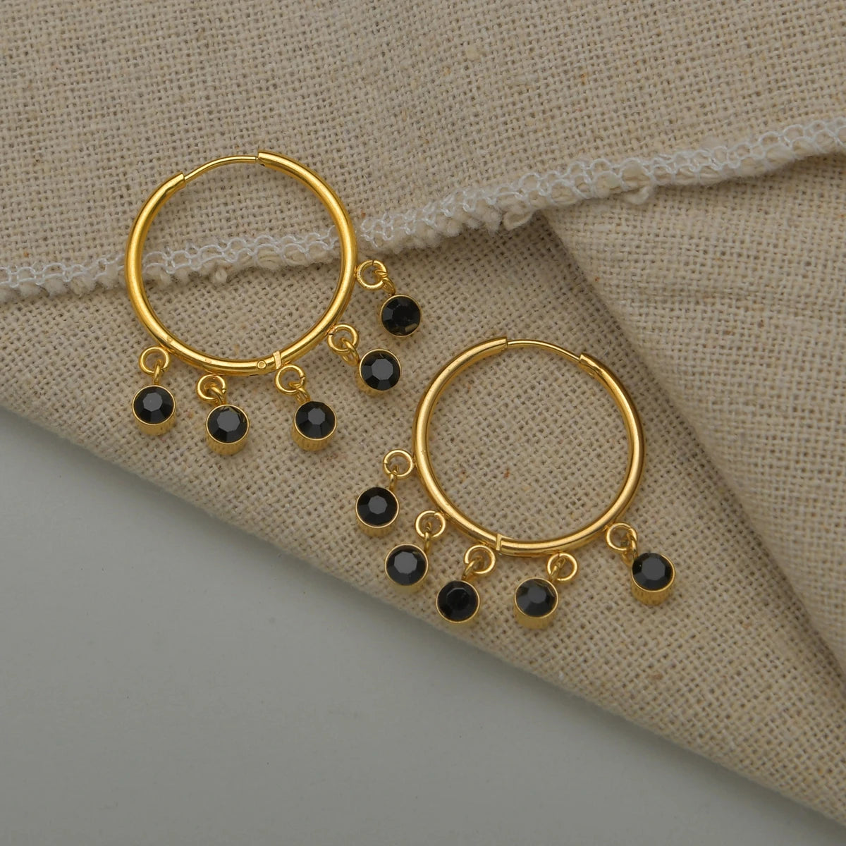 Gold hoop earrings with black beads on a beige fabric background
