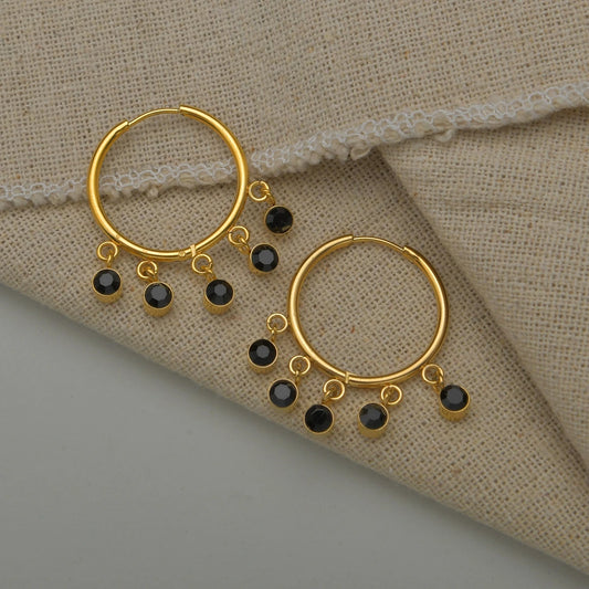 Gold hoop earrings with black beads on a beige fabric background