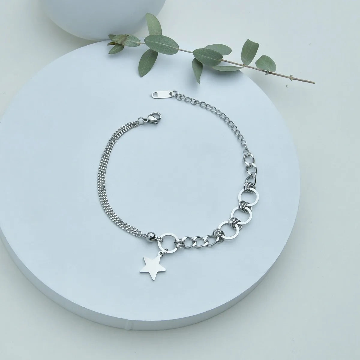 Silver bracelet with a star charm on a white surface with green leaves.