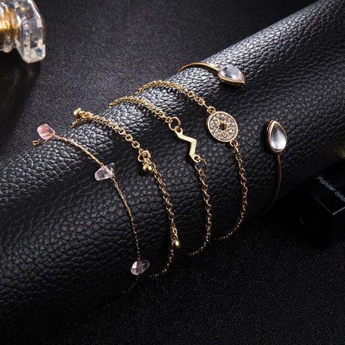 Gold bracelets with gemstone charms on a black leather surface