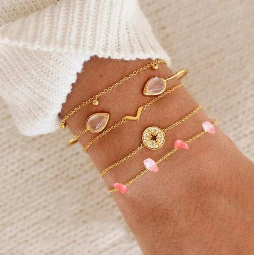 Gold bracelet set with pink stones on a person's bracelet against a neutral background