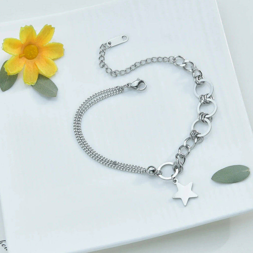 Silver bracelet with star charm on a white surface with a yellow flower and green leaves.
