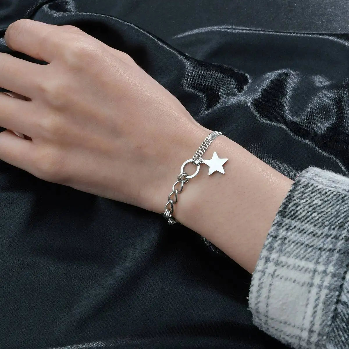 Silver bracelet with star charm on a wrist against a dark fabric background