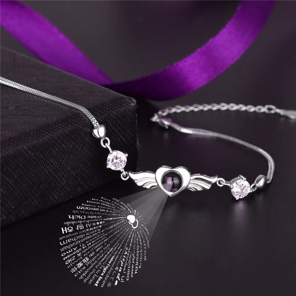 Silver bracelet with heart and wing design on a dark surface with purple ribbon