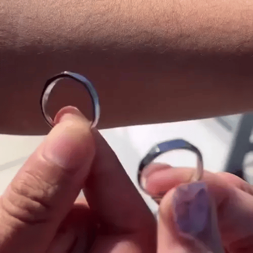 Close-up of a hand holding a small Light Sculpted Couple Rings Set against a arm