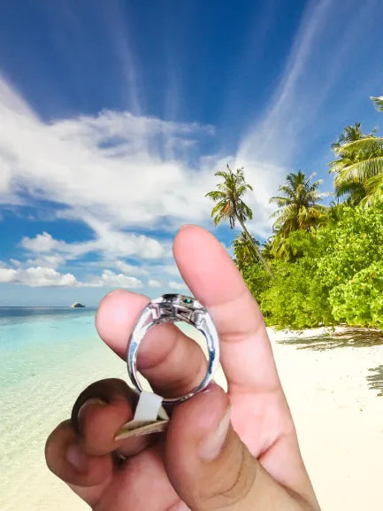 Hand holding a silver ring with a tropical beach in the background
