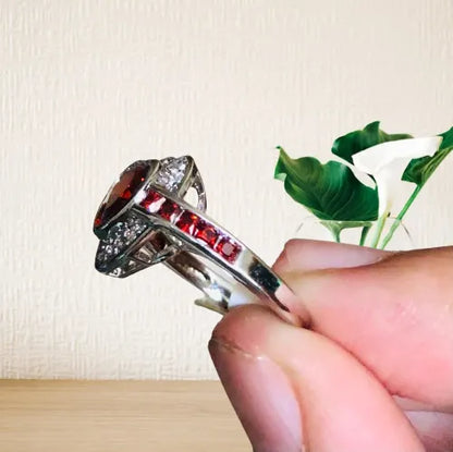 Silver ring with red gemstone held by a hand against a neutral background
