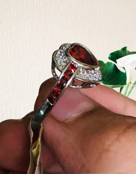 Silver ring with red gemstones held by a hand against a light background