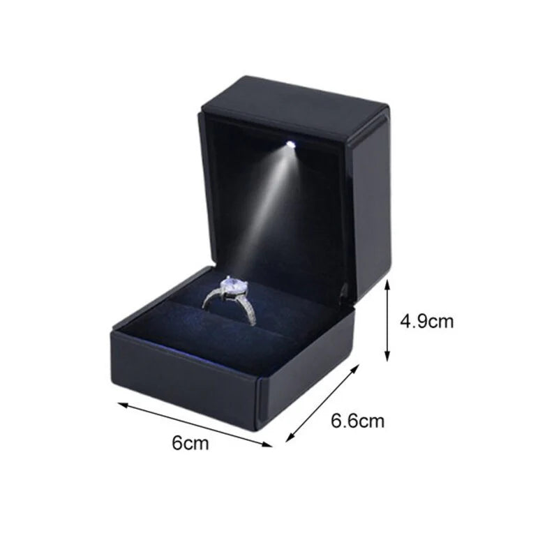 Black jewelry box with a ring inside, illuminated by a light source, on a white background.
