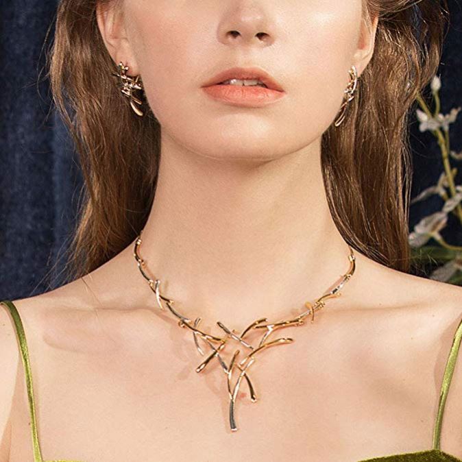 Woman wearing a gold necklace with a green top against a dark background