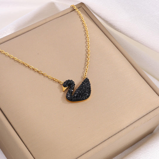 Gold necklace with a black swan pendant on a beige box