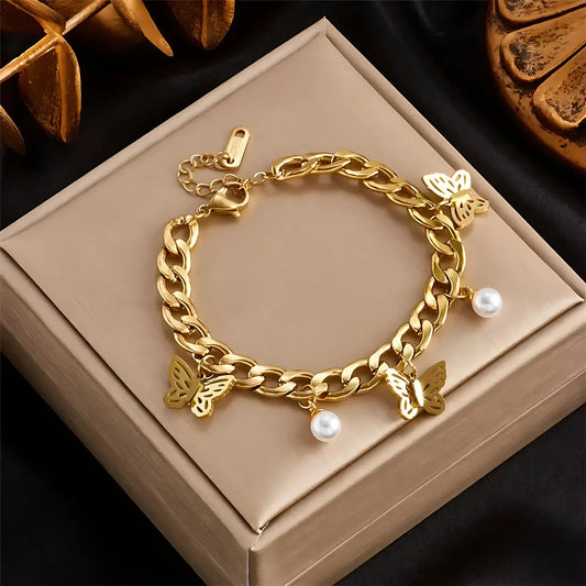 Gold chain bracelet with butterfly and pearl charms on a beige box