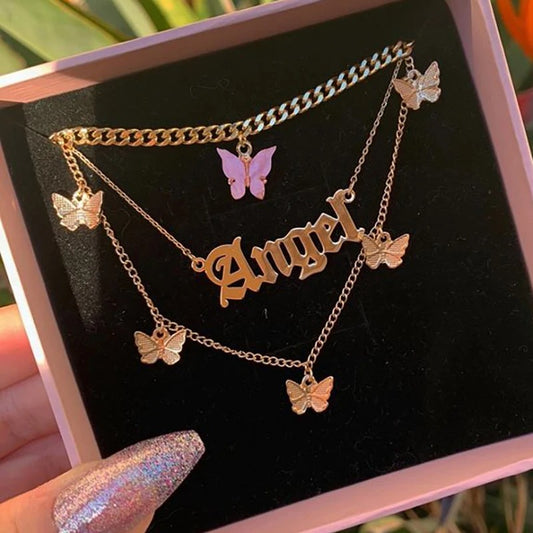 Gold necklace with 'Angel' pendant and butterfly charms on a black display box.