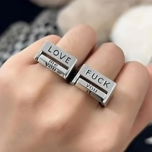 Silver ring with 'LOVE me' and 'FUCK it' text on a ring finger.